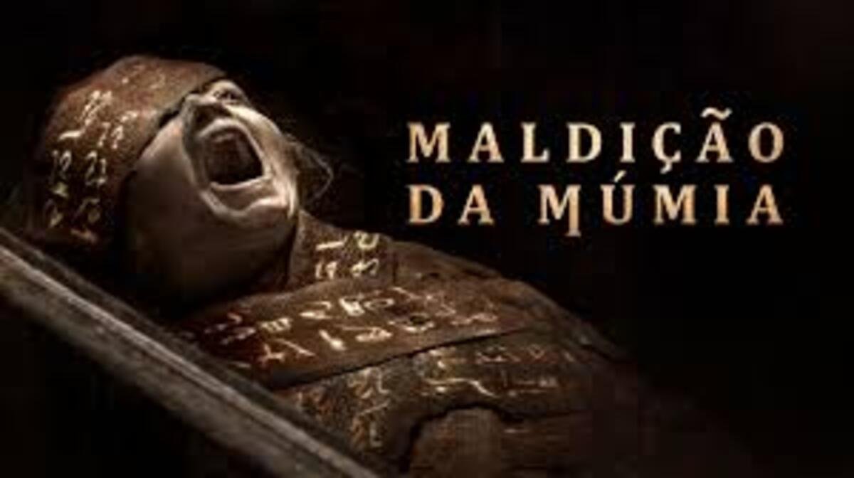 Imagem em tons escuros e dourados mostrando uma múmia antiga deitada de perfil dentro de um sarcófago inclinado. A cabeça da múmia está enfaixada com tecidos rústicos cobertos por inscrições e símbolos antigos, e sua boca está aberta em uma expressão fixa de grito ou agonia. À direita, sobre o fundo preto e sombrio, o título Maldição da Múmia está escrito com letras maiúsculas douradas em uma fonte estilizada que remete a inscrições em pedra.