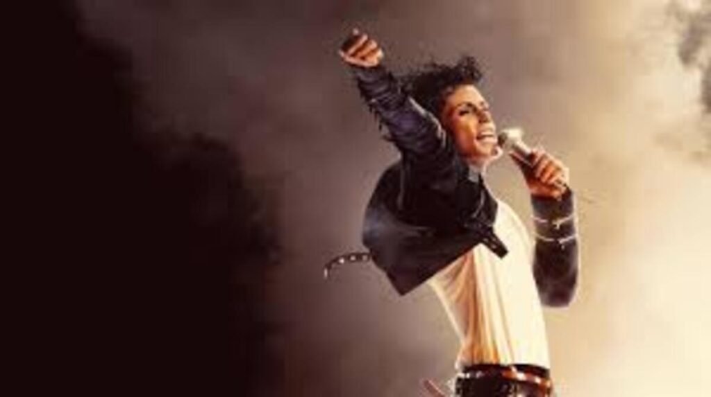 Cena da cinebiografia 'Michael' com o ator Jaafar Jackson caracterizado como Michael Jackson em uma performance de palco. A imagem captura a energia e o estilo icônico do Rei do Pop em um cenário de show
