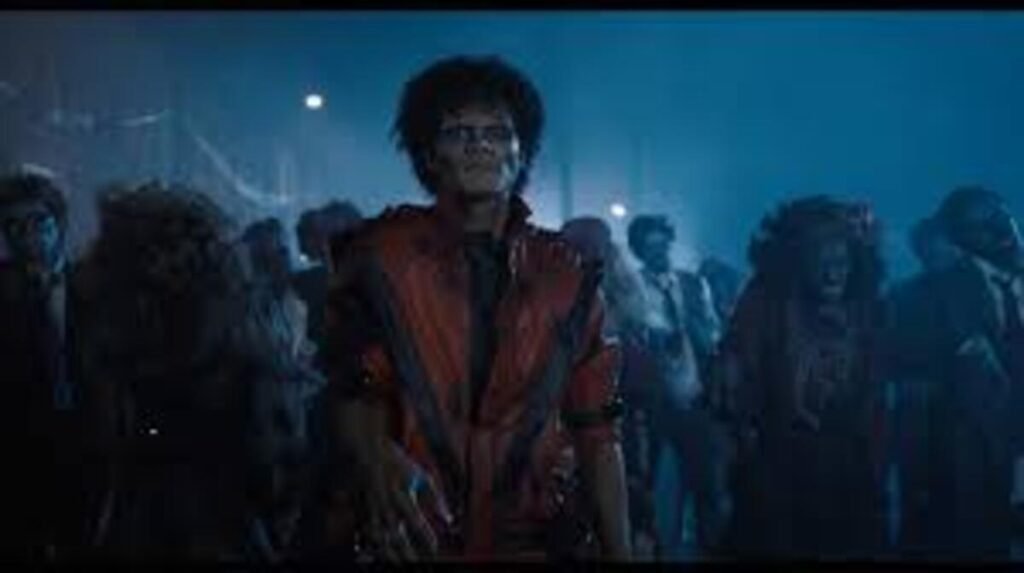 Cena da cinebiografia 'Michael' recriando o videoclipe Thriller. O protagonista aparece vestido com a jaqueta vermelha clássica e maquiagem de zumbi, liderando um exército de mortos-vivos em um cenário escuro e enevoado