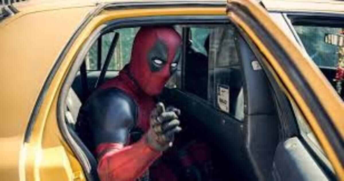 O personagem Deadpool, vestindo seu traje tático vermelho e preto, aparece sentado no banco traseiro de um táxi amarelo. Ele está com o corpo inclinado para frente e aponta um dedo diretamente para a câmera através da porta aberta do veículo, com uma expressão sugerida pela máscara de confiança e sarcasmo.