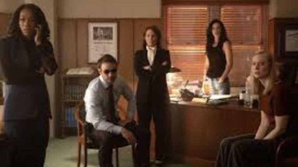 Personagens das séries Demolidor e Jessica Jones reunidos em um escritório em momento de tensão dramática.