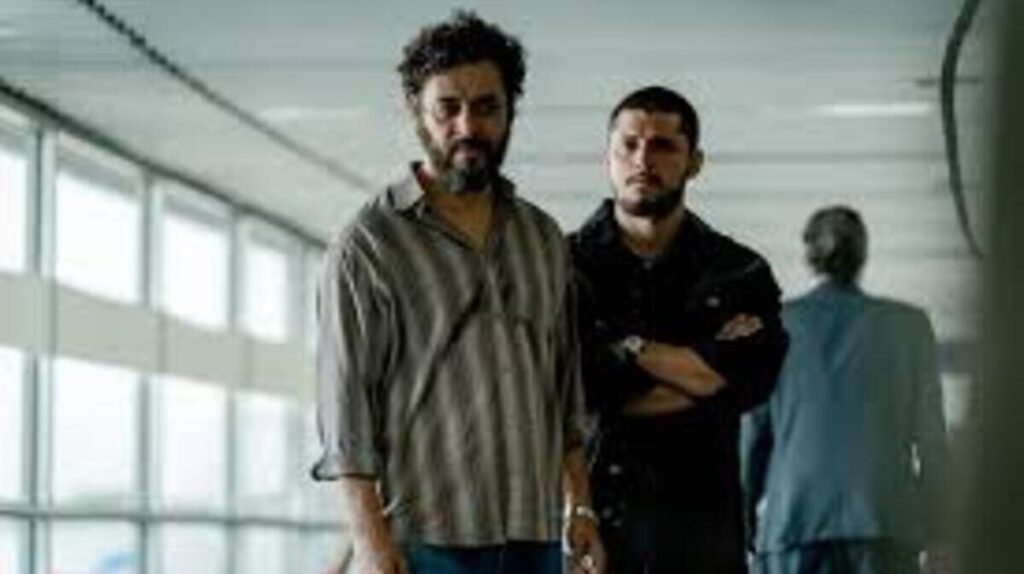 Cena da série brasileira Impuros mostrando dois personagens em um ambiente que parece ser um aeroporto ou prédio governamental. A imagem captura um momento de tensão e seriedade entre os protagonistas da produção.