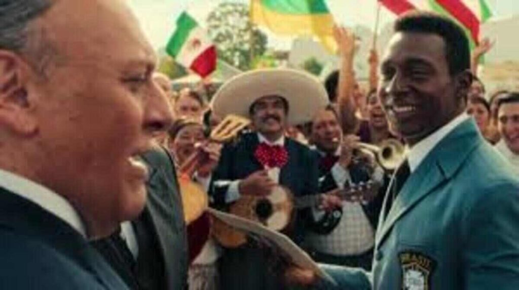 Crítica | Brasil 70 – A Saga do Tri: O gol de placa da Netflix que une futebol e ditadura militar 5 Ator interpretando Pelé com terno oficial da seleção durante recepção calorosa com mariachis no México. A imagem da série Brasil Setenta A Saga do Tri destaca a ambientação festiva e cultural da época, sendo perfeita para ilustrar análises de fidelidade histórica, críticas de episódios e listas de produções sobre futebol no site.