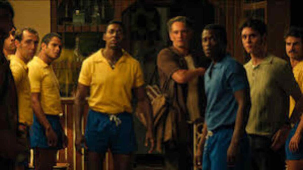 Crítica | Brasil 70 – A Saga do Tri: O gol de placa da Netflix que une futebol e ditadura militar 4 Elenco caracterizado em momento de grande tensão e expectativa nos bastidores da série dramática Brasil Setenta A Saga do Tri. A imagem promocional focada na reação coletiva e na ambientação realista de época é ideal para ilustrar análises de roteiro, críticas de episódios marcantes e listas de produções sobre a história do futebol brasileiro no site.