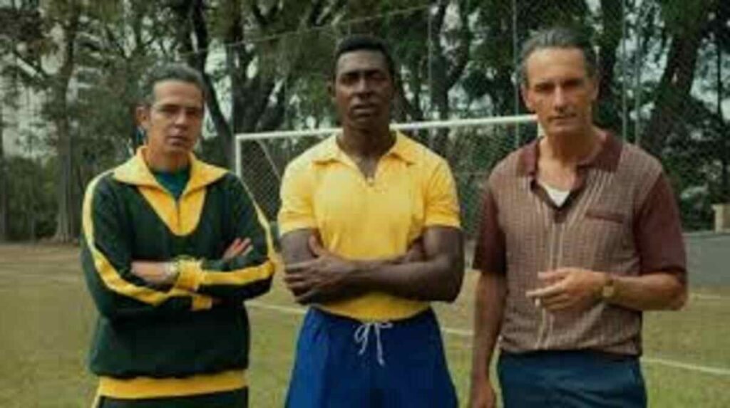 Crítica | Brasil 70 – A Saga do Tri: O gol de placa da Netflix que une futebol e ditadura militar 2 Atores caracterizados em cena de reconstituição histórica no gramado para a série documental Brasil Setenta A Saga do Tri. A imagem promocional destacando o figurino esportivo de época, a ambientação clássica e os personagens que marcaram os bastidores do futebol nacional é ideal para ilustrar críticas de episódios, análises de produções brasileiras e listas de séries sobre esporte.