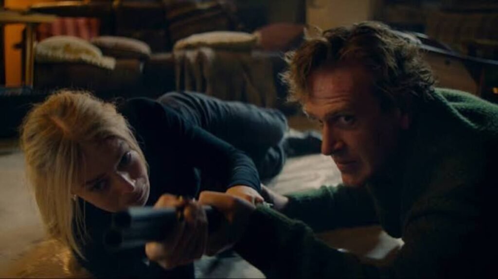 Casal protagonista armado e deitado no chão em momento de grande tensão e perigo na trama do filme Por Cima do Seu Cadáver. A imagem promocional destacando o clima de invasão doméstica, suspense psicológico e sobrevivência é ideal para ilustrar críticas de cinema, análises de cenas de ação e novidades sobre thrillers no blog.