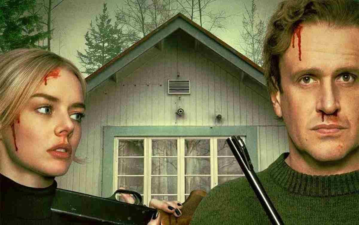 Casal protagonista ferido e armado em frente a uma cabana isolada no pôster oficial do filme Por Cima do Seu Cadáver. A arte de divulgação focada no clima de suspense, perigo iminente e thriller psicológico é perfeita para ilustrar críticas de cinema, resumos de tramas de mistério e análises de lançamentos no blog.