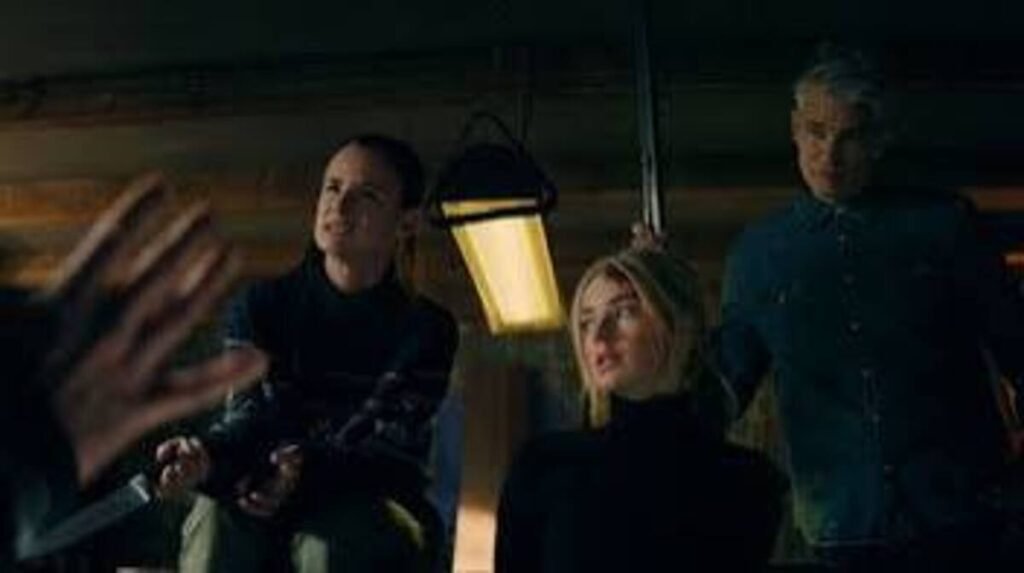 Grupo de personagens reunidos em cativeiro ou esconderijo sob luz tensa em cena de grande mistério do filme Por Cima do Seu Cadáver. A imagem promocional de forte apelo visual e clima de suspense psicológico é perfeita para ilustrar críticas cinematográficas, resumos de arcos narrativos e posts sobre thrillers no blog.