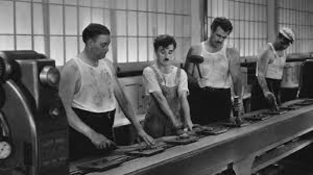 Tempos Modernos (1936): A Crítica de Charlie Chaplin à Grande Depressão e ao Fordismo 4 Charles Chaplin trabalhando em uma linha de montagem acelerada no filme Tempos Modernos. A imagem clássica em preto e branco que retrata a crítica social ao trabalho industrial repetitivo e à produção em massa é ideal para ilustrar análises cinematográficas, posts sobre a história do cinema mudo e listas de grandes obras no site.