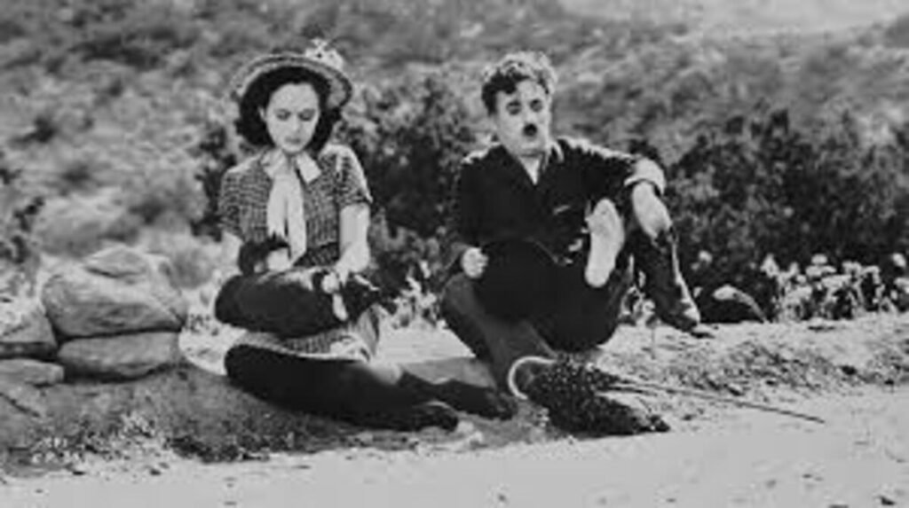 Tempos Modernos (1936): A Crítica de Charlie Chaplin à Grande Depressão e ao Fordismo 3 Charles Chaplin e Paulette Goddard em uma cena clássica de estrada no filme Tempos Modernos. A imagem em preto e branco que retrata a jornada e o companheirismo dos personagens com o humor característico do cinema mudo é excelente para ilustrar críticas detalhadas, análises de narrativa visual e listas de clássicos marcantes no site.