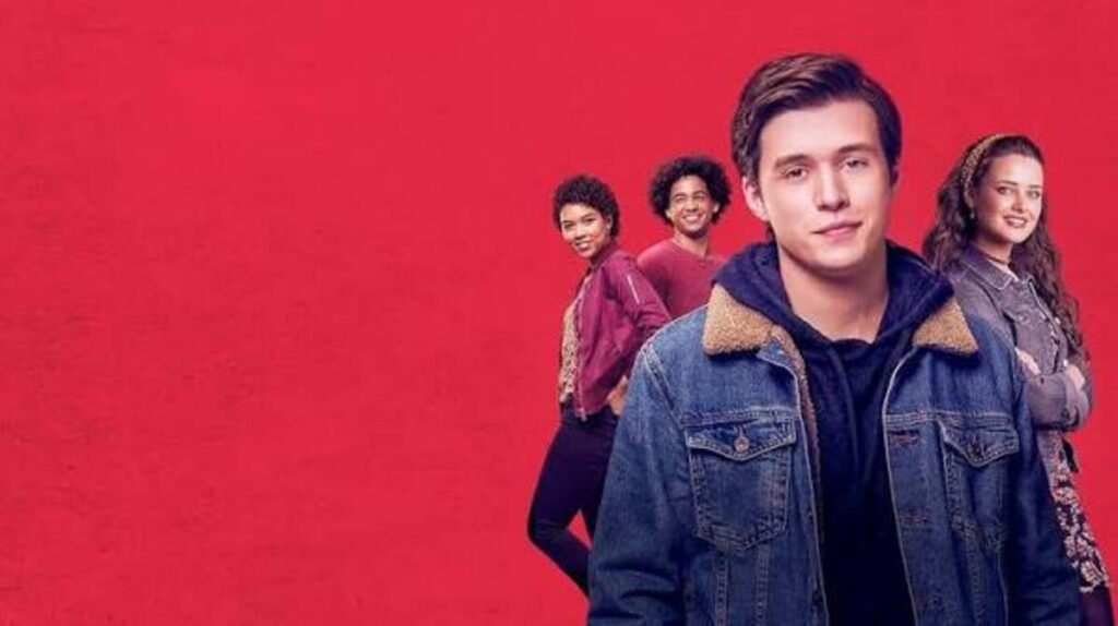 Filmes de amadurecimento: As produções contemporâneas que explicam a nova geração 8 Nick Robinson de jaqueta jeans em primeiro plano com elenco ao fundo sobre um fundo vermelho vibrante em pôster do filme Com Amor, Simon.