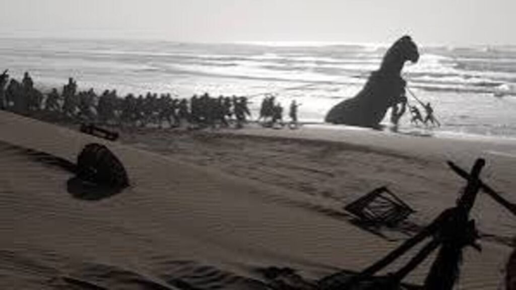 Dezenas de soldados puxando a silhueta do gigantesco Cavalo de Tróia na beira do mar em foto épica em preto e branco do filme A Odisseia.