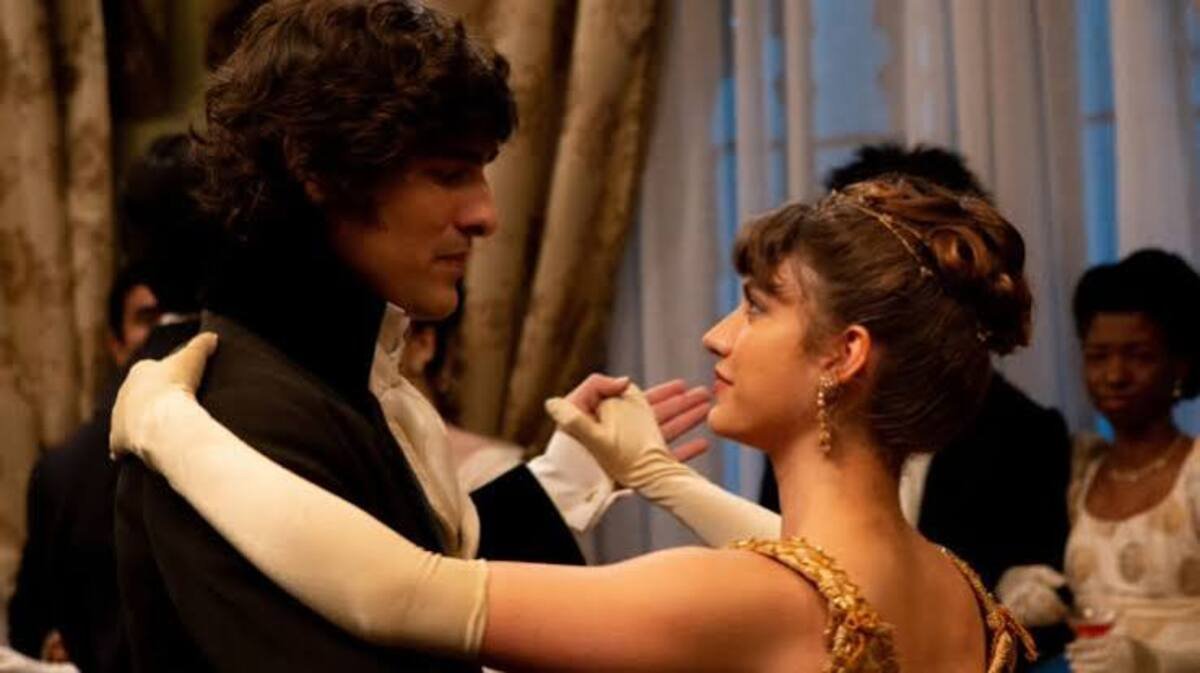 Casal de protagonistas dançando romanticamente em salão de festas durante cena de famosa série de drama e romance de época. A imagem capturando a atmosfera clássica e o figurino elegante é ideal para ilustrar críticas de episódios, guias de maratona e análises de produções românticas no site.