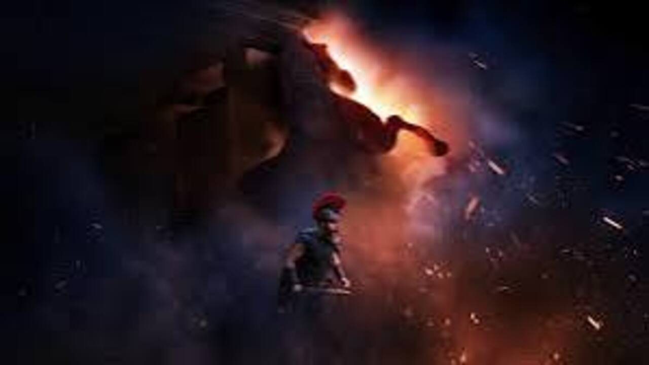Guerreiro com elmo de pluma vermelha caminha em meio a faíscas de fogo diante do gigantesco Cavalo de Tróia em cena do filme A Odisseia.