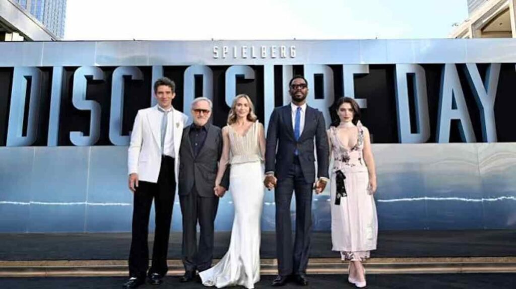 Crítica | Dia D (2026): O novo filme de ficção científica de Steven Spielberg decepciona? 3 Steven Spielberg e o elenco principal de trajes de gala posam de mãos dadas em frente ao imenso letreiro oficial de Disclosure Day em evento de tapete vermelho.